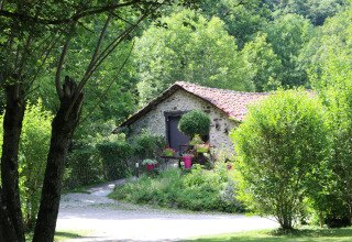 Stone cottage with red tiled roof surrounded by lush greenery at Moulin de Chaules campsite, France.