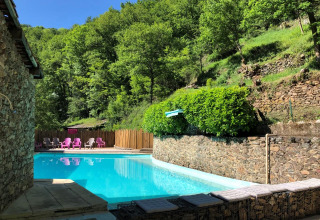 Piscina esterna del campeggio Moulin de Chaules, circondata dal verde e sedie colorate sullo sfondo.