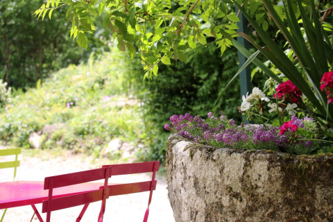 Sedie e tavolo colorati accanto a una fioriera in pietra in un'area verde del campeggio Moulin de Chaules.