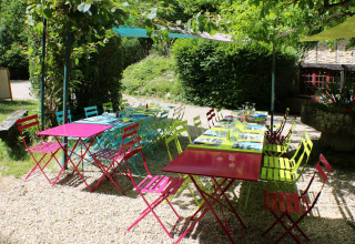 Colorful outdoor tables and chairs under greenery at Campsite Moulin de Chaules in Auvergne-Rhône-Alpes, France.