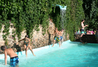 Bambini giocano in piscina con cascata al campeggio Moulin de Chaules, Alvernia-Rodano-Alpi, Francia.