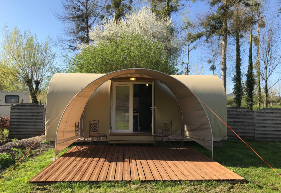 Cocosweet safaritent met overdekt houten terras, twee stoelen en groene omgeving op een zonnige dag.