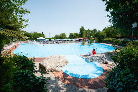 Piscina al aire libre en el Centro Vacanze San Marino, rodeada de sillas, vegetación y familias disfrutando.
