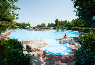 Piscina all'aperto al Centro Vacanze San Marino, circondata da sdraio, rocce, alberi e famiglie al sole.