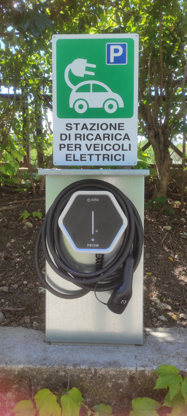 Elbil opladningsstation i Centro Vacanze San Marino feriested, omkranset af grønne planter og træer.