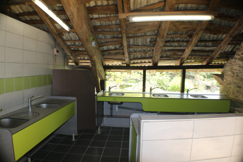 Communal kitchen area with multiple sinks and green counters at Campsite Moulin de Chaules, Auvergne, France.