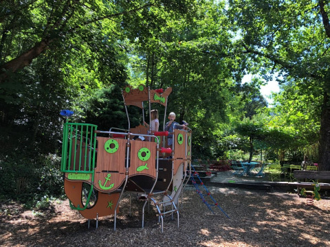 Children playing on a pirate ship playground surrounded by trees at Campsite Moulin de Chaules in France.