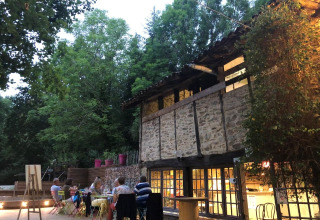 Zona pranzo all'aperto al campeggio Moulin de Chaules, con ospiti che cenano vicino a un edificio rustico.