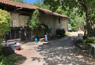 Outdoor view of Campsite Moulin de Chaules with stone building, seating, and trees in Auvergne, France.