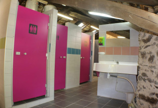 Bagni comuni con porte rosa e lavandino al campeggio Moulin de Chaules in Alvernia-Rodano-Alpi, Francia.