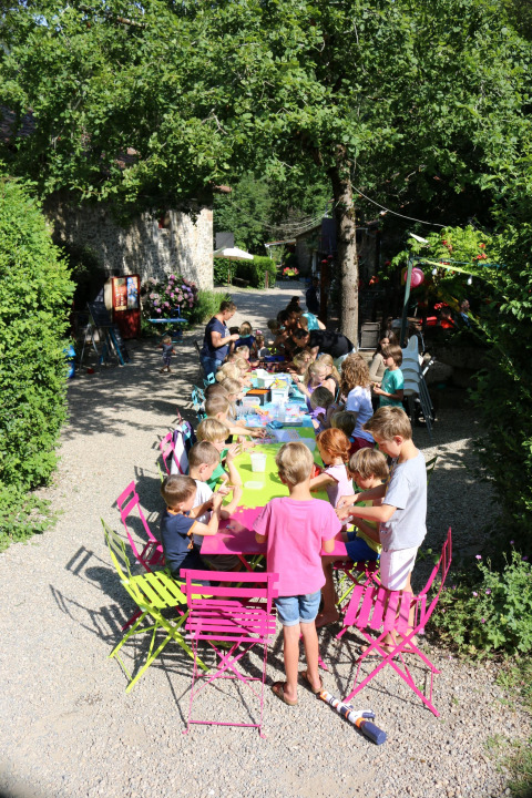 Bambini seduti a un tavolo colorato all'aperto al campeggio Moulin de Chaules in Francia.