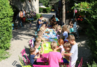 Bambini seduti a un tavolo colorato all'aperto al campeggio Moulin de Chaules in Francia.