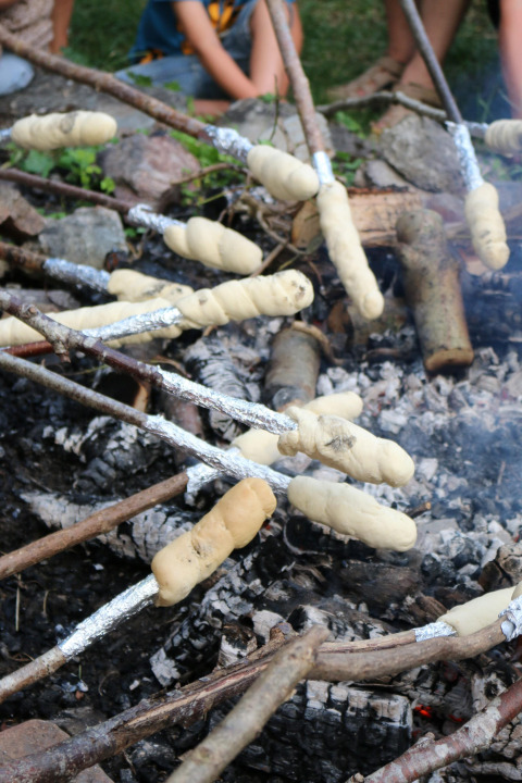 Children roasting dough on sticks over a campfire at Moulin de Chaules campsite in Auvergne, France.