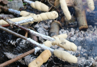 Children roasting dough on sticks over a campfire at Moulin de Chaules campsite in Auvergne, France.