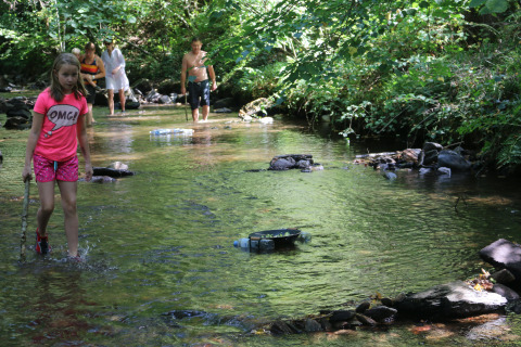 Children and adults wade in a shallow creek at Campsite Moulin de Chaules, a holiday park in France.