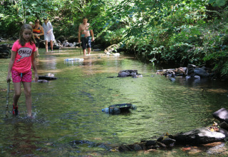 Children and adults wade in a shallow creek at Campsite Moulin de Chaules, a holiday park in France.
