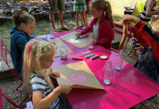 Bambini fanno attività artistiche all'aperto su un tavolo rosa al campeggio Moulin de Chaules, Francia.