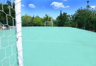 Campo de fútbol exterior en Centro Vacanze San Marino, rodeado de árboles y cielo azul despejado.