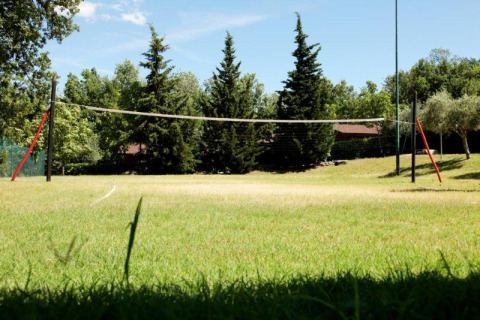 Cancha de voleibol al aire libre en Centro Vacanze San Marino, rodeada de árboles y césped verde.
