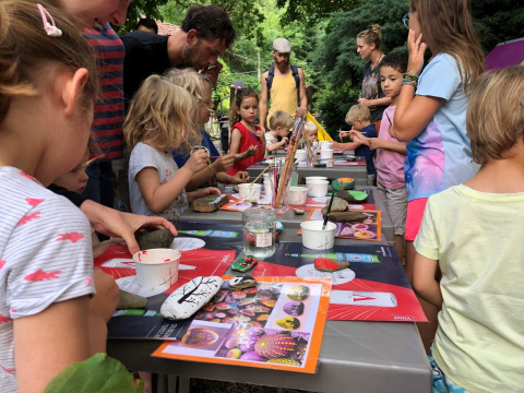 Bambini e adulti dipingono sassi insieme all'aperto al campeggio Moulin de Chaules in Francia.