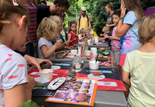 Children and adults painting rocks together outdoors at Campsite Moulin de Chaules holiday park in France.