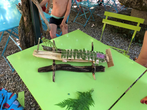 Bambini giocano all'aperto a un tavolo con una barca fatta di legno e foglie in un campeggio in Francia.