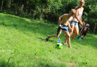 Bambini e adulti giocano a calcio sull’erba al Camping Moulin de Chaules in Alvernia-Rodano-Alpi, Francia.
