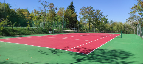 Udendørs tennisbane på Centro Vacanze San Marino feriested, omgivet af grønne træer under blå himmel.