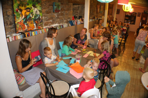 Bambini e adulti fanno attività creative ai tavoli di un vivace caffè al campeggio Moulin de Chaules, Francia.