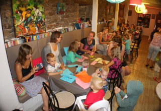 Children and adults doing crafts at tables in a lively café at Campsite Moulin de Chaules in France.