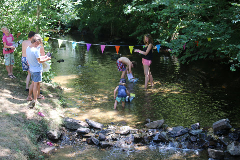 Families enjoy playing in a shallow stream at Campsite Moulin de Chaules holiday park, Auvergne-Rhône-Alpes, France.
