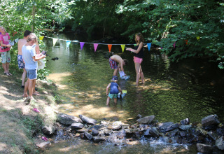 Families enjoy playing in a shallow stream at Campsite Moulin de Chaules holiday park, Auvergne-Rhône-Alpes, France.