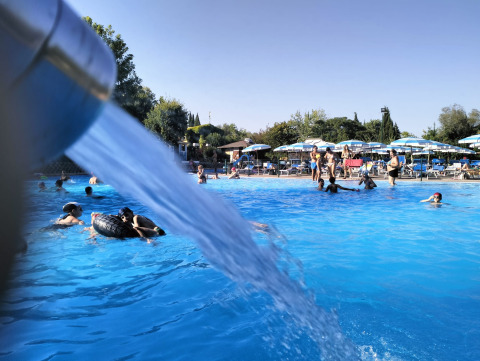 Folk nyder en solrig dag ved poolen i Centro Vacanze San Marino, med springvand og parasoller i baggrunden.