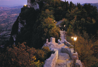 Verlichte stenen wandelweg slingert door groen en leidt naar een kasteel op een heuveltop in San Marino.