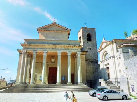 La majestueuse basilique de San Marino avec sa façade à colonnes, son clocher et des visiteurs devant.