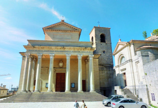La majestueuse basilique de San Marino avec sa façade à colonnes, son clocher et des visiteurs devant.