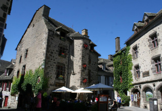 Stone buildings and a café at Moulin de Chaules campsite, a holiday park in Auvergne-Rhône-Alpes, France, on a sunny day.