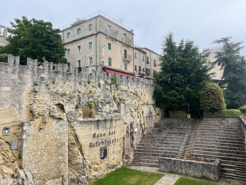 Amphithéâtre en pierre et remparts historiques à Saint-Marin, entourés d’arbres et de bâtiments anciens.