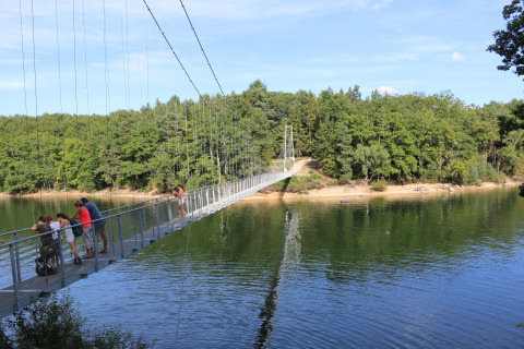 People walking on a suspension bridge over a calm river near Saint Constant, Auvergne-Rhône-Alpes, France.