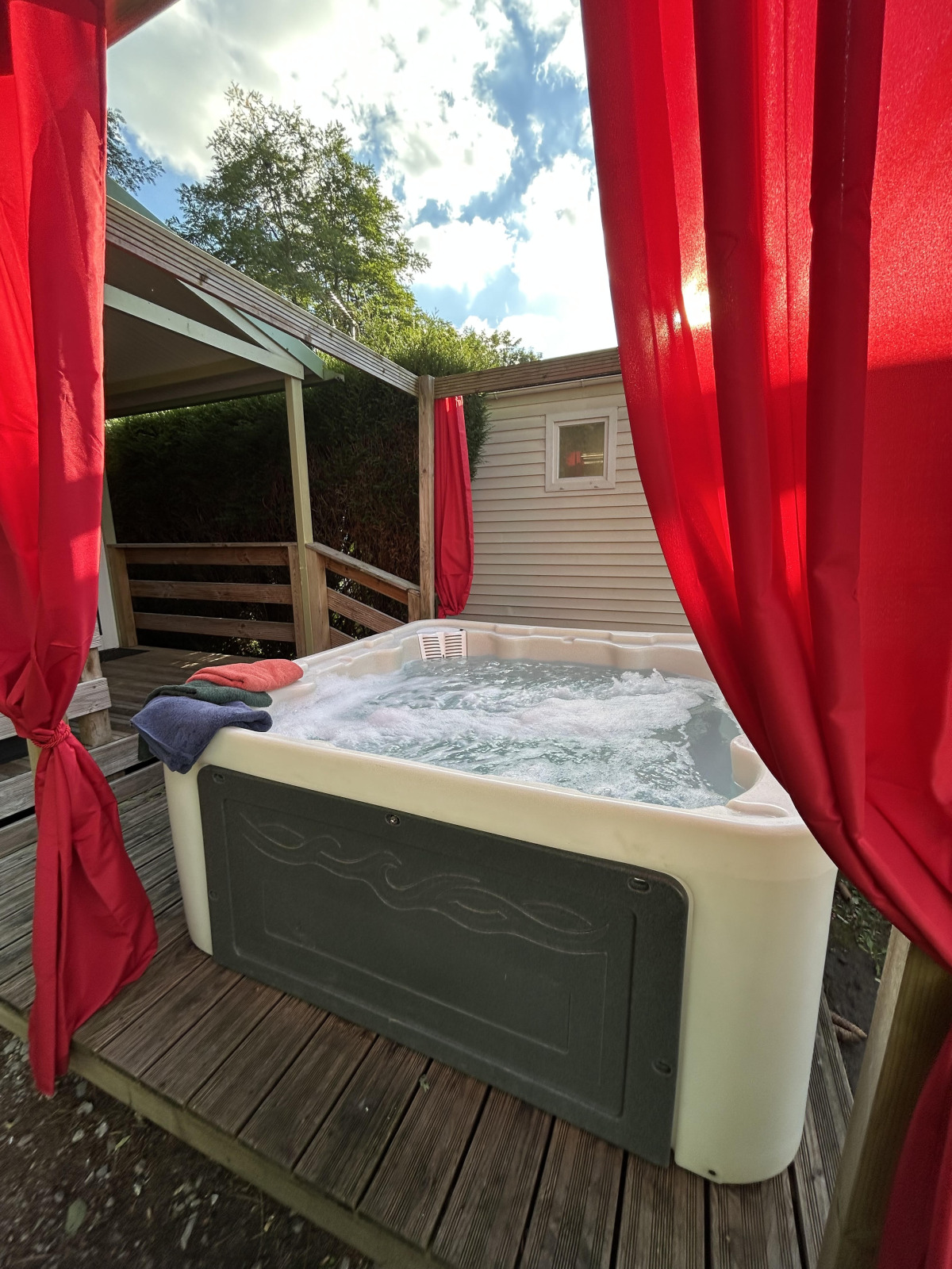 Bubbelend buitenjacuzzi met rode gordijnen bij Chalet du Bélier, Flower Camping de la Trye, Frankrijk.