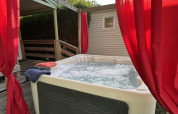 Bubbelend buitenjacuzzi met rode gordijnen bij Chalet du Bélier, Flower Camping de la Trye, Frankrijk.