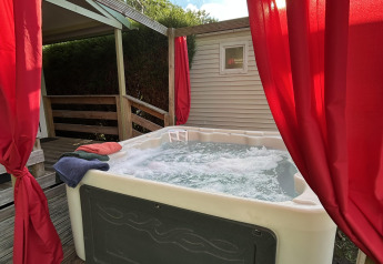 Udendørs jacuzzi med bobler og røde gardiner ved Chalet du Bélier på Flower Camping de la Trye i Frankrig.