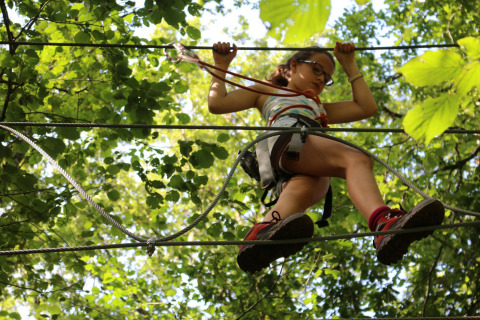 Child wearing a harness crosses ropes on a treetop adventure course near Saint Constant, Auvergne-Rhône-Alpes.