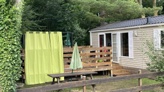 Buiten bij Bungalow du Parc + jacuzzi met houten terras, picknicktafel, groene gordijnen en omringende bomen.