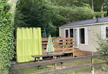 Outdoor view of Bungalow du Parc + jacuzzi with wooden deck, picnic table, green curtains, and trees.