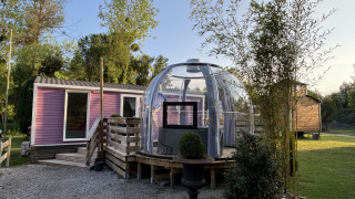 Buitenjacuzzi in een glazen bol bij een paarse bungalow van Bungalow La Folle Entreprise, omgeven door groen.