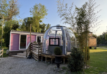 Jacuzzi extérieur sous dôme transparent à côté d’un bungalow violet au Bungalow La Folle Entreprise, entouré de verdure.