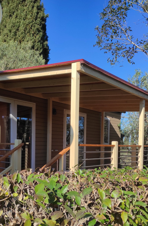 Casa mobile «Riviera» al Centro Vacanze San Marino, veranda in legno e siepi verdi in primo piano.