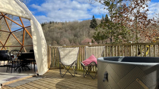 Terraza de Dôme Lodge Spa con carpa cúpula, jacuzzi, sillas plegables y vistas a colinas boscosas.