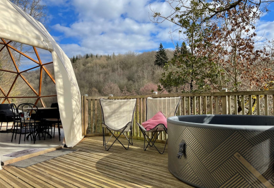Terras aan Dôme Lodge Spa met een koepeltent, bubbelbad, zetels en uitzicht op beboste heuvels.